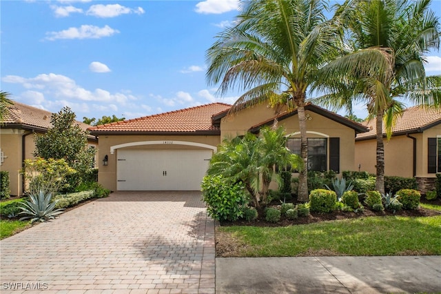 mediterranean / spanish-style house featuring a tiled roof, decorative driveway, an attached garage, and stucco siding