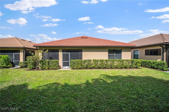 back of house featuring a tile roof, a lawn, and stucco siding