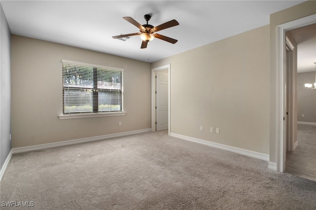 carpeted spare room featuring baseboards and ceiling fan with notable chandelier