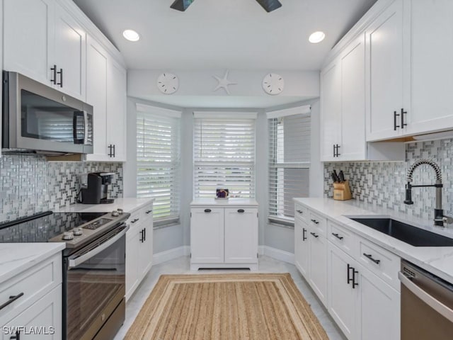 kitchen featuring light stone counters, stainless steel appliances, backsplash, white cabinetry, and a sink