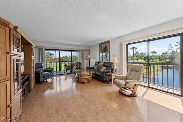 living room with a water view, a textured ceiling, and light wood finished floors