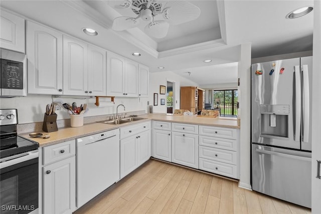 kitchen featuring light wood-style flooring, a sink, a tray ceiling, stainless steel appliances, and white cabinets