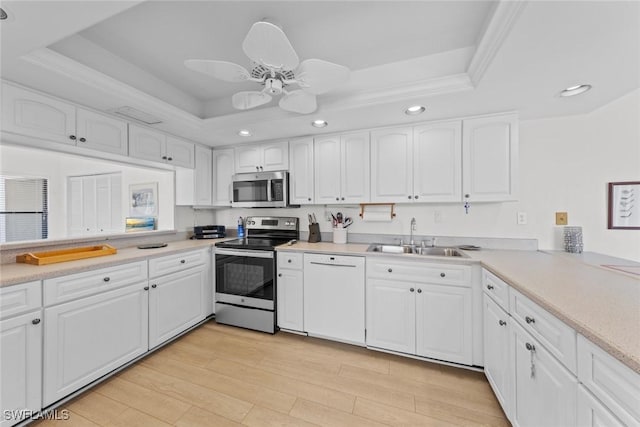 kitchen with light wood-style flooring, a sink, stainless steel appliances, white cabinets, and a raised ceiling