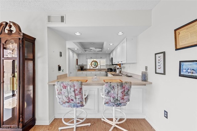 kitchen featuring a tray ceiling, visible vents, a peninsula, and light wood-style flooring