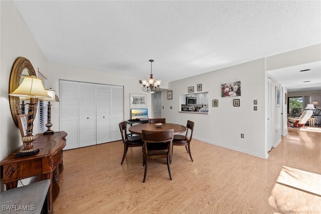 dining area with a chandelier, baseboards, a textured ceiling, and light wood-style flooring