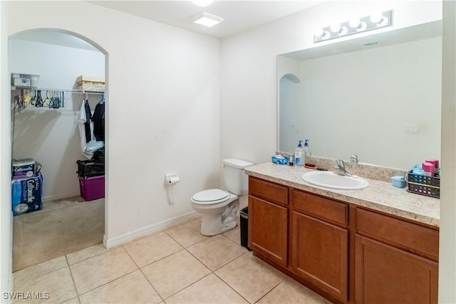 bathroom with toilet, tile patterned flooring, vanity, and a walk in closet