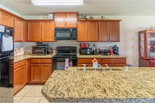 kitchen with light tile patterned floors, a toaster, a sink, light stone countertops, and black appliances