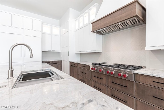 770 Port Side Dr, Naples, FL 34103 - kitchen with custom exhaust hood, stainless steel gas stovetop, tasteful backsplash, white cabinets, and light stone counters