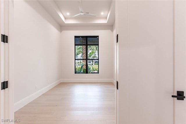 empty room with recessed lighting, light wood-style flooring, baseboards, and a raised ceiling
