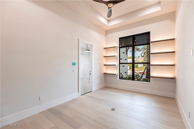 spare room featuring a tray ceiling, light wood-style floors, ceiling fan, and baseboards