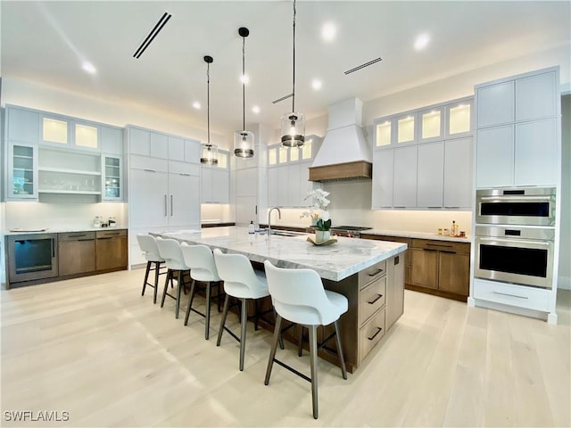 770 Port Side Dr, Naples, FL 34103 - kitchen with custom exhaust hood, stainless steel double oven, light wood finished floors, a kitchen breakfast bar, and recessed lighting
