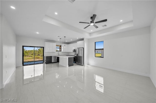 unfurnished living room featuring a tray ceiling, a healthy amount of sunlight, and visible vents