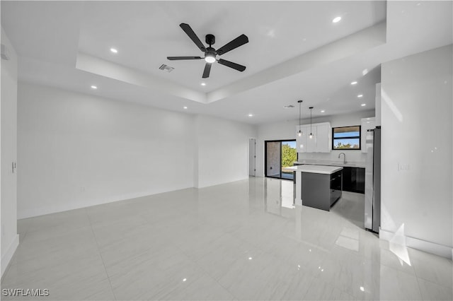 unfurnished living room with a tray ceiling, recessed lighting, visible vents, a ceiling fan, and a sink