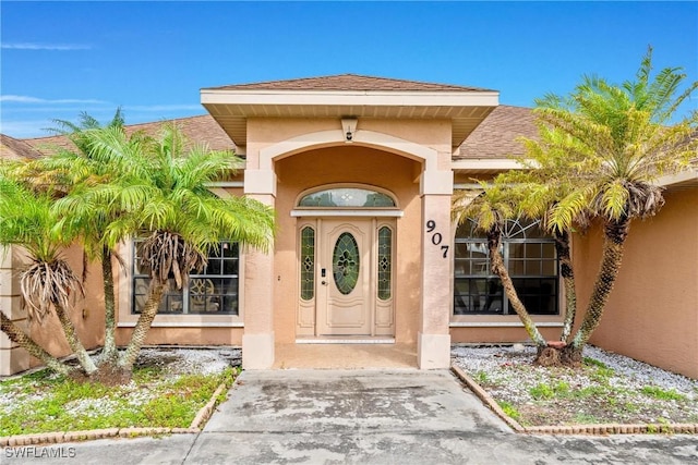 entrance to property with a shingled roof and stucco siding