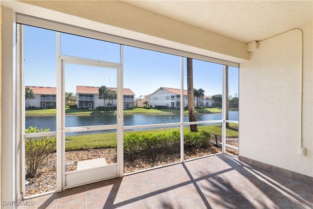 unfurnished sunroom featuring a water view, a healthy amount of sunlight, and a residential view