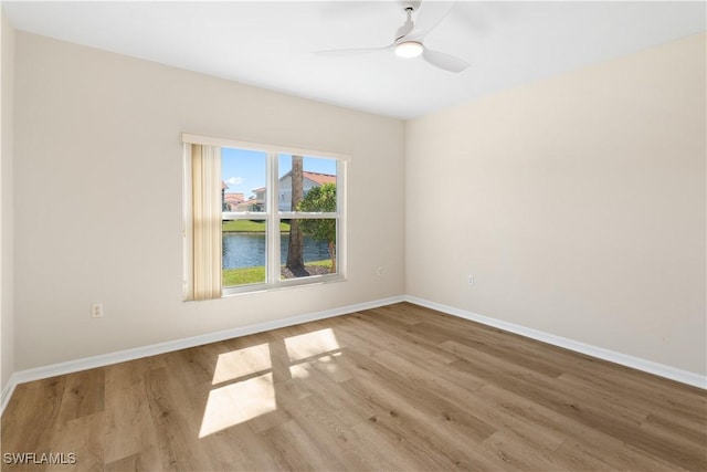 spare room with a ceiling fan, a water view, baseboards, and wood finished floors