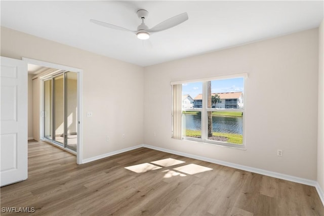 empty room with a water view, wood finished floors, a ceiling fan, and baseboards