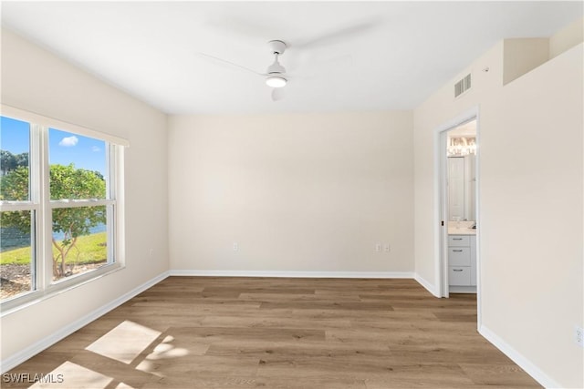 spare room featuring light wood-style flooring, a ceiling fan, visible vents, and baseboards