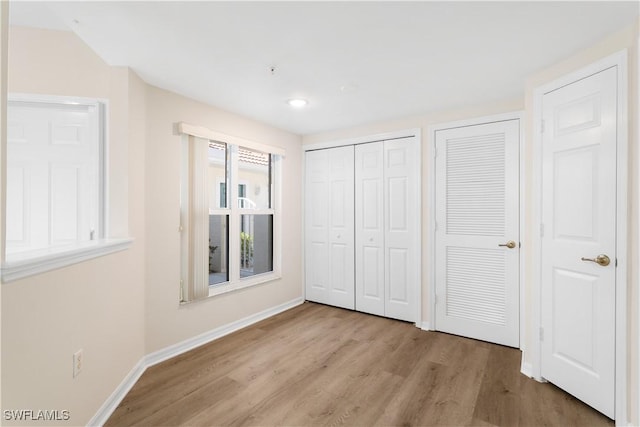 unfurnished bedroom featuring two closets, baseboards, and wood finished floors