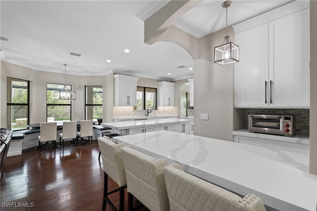 kitchen with a toaster, tasteful backsplash, white cabinets, ornamental molding, and dark wood-style flooring