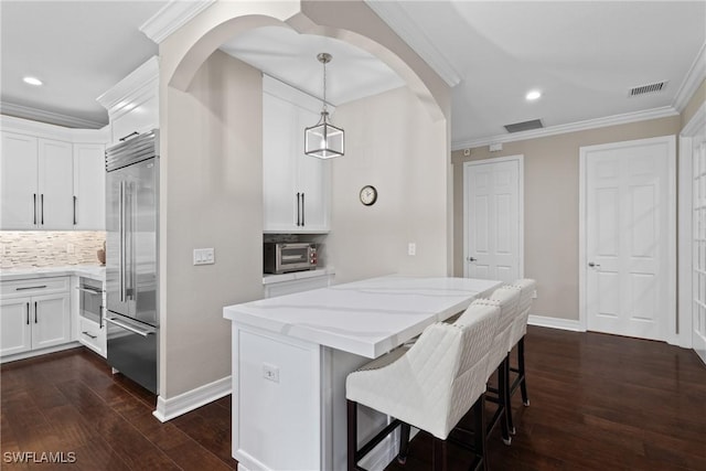 kitchen with visible vents, dark wood-style floors, ornamental molding, built in refrigerator, and light stone countertops