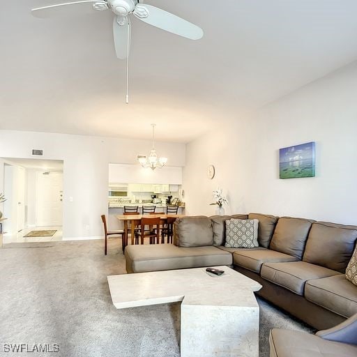 living room featuring carpet floors, baseboards, and ceiling fan with notable chandelier