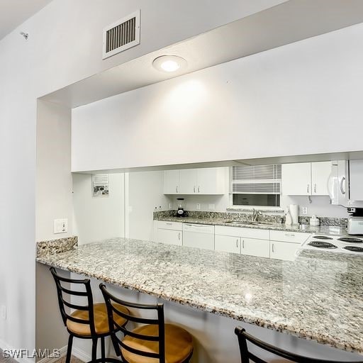 kitchen with light stone counters, visible vents, a sink, and a peninsula