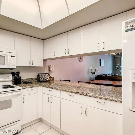 kitchen featuring white appliances, white cabinetry, light stone counters, and light tile patterned flooring