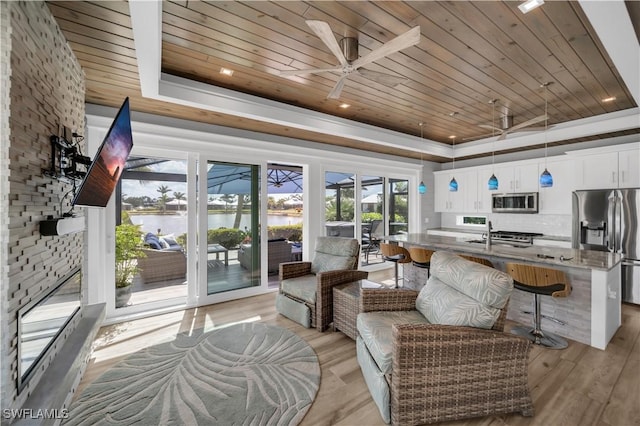 sunroom / solarium featuring a sink, a tray ceiling, wood ceiling, and a ceiling fan