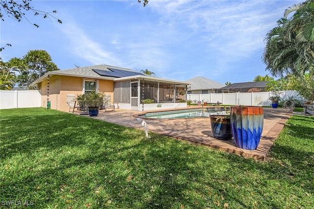 back of house featuring a sunroom, a fenced backyard, a lawn, and roof mounted solar panels