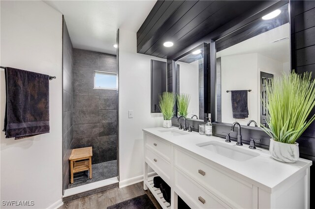 bathroom with wood finished floors, double vanity, a sink, and walk in shower