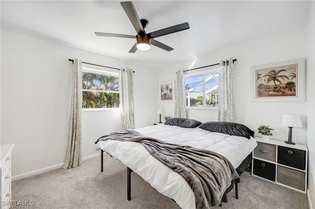 bedroom featuring a ceiling fan, light colored carpet, multiple windows, and baseboards