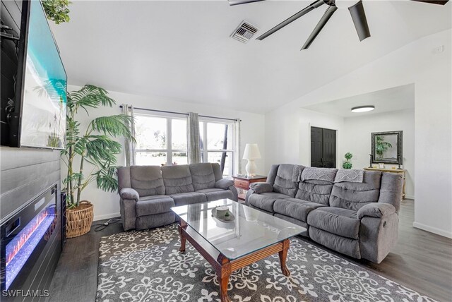 living room with visible vents, a glass covered fireplace, ceiling fan, wood finished floors, and vaulted ceiling