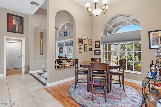 tiled dining space featuring an inviting chandelier, baseboards, a high ceiling, and visible vents