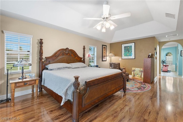 bedroom with arched walkways, wood finished floors, a raised ceiling, and visible vents