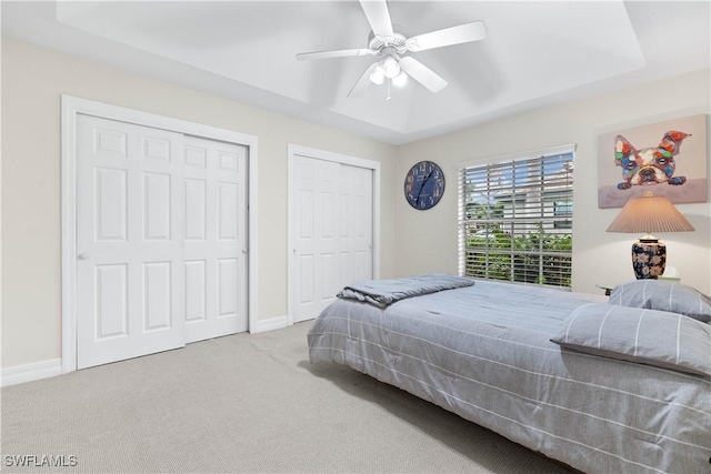 carpeted bedroom featuring a tray ceiling, two closets, a ceiling fan, and baseboards