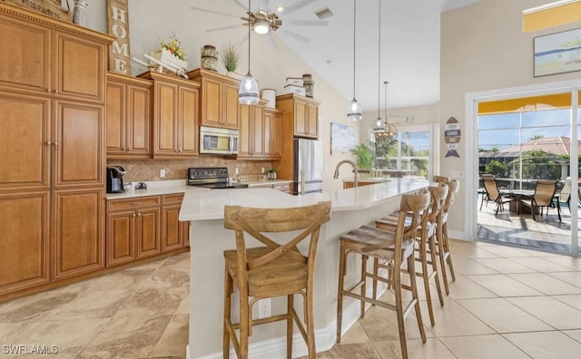 kitchen featuring stainless steel appliances, light countertops, backsplash, brown cabinets, and an island with sink