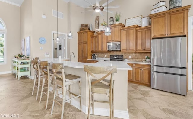 kitchen featuring visible vents, brown cabinetry, an island with sink, stainless steel appliances, and light countertops