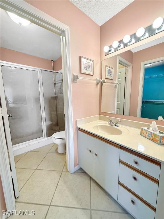 bathroom featuring a stall shower, toilet, tile patterned flooring, a textured ceiling, and vanity