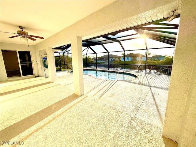 pool with a patio area, glass enclosure, and a ceiling fan