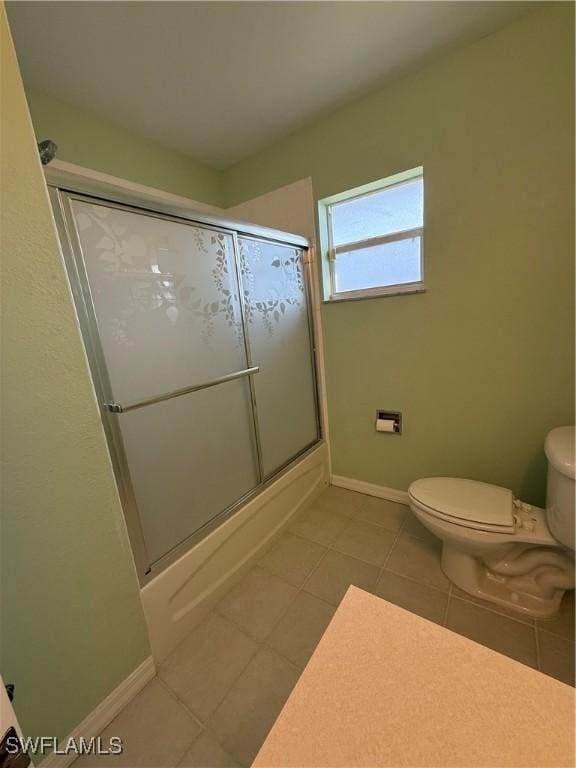 bathroom featuring toilet, shower / bath combination with glass door, baseboards, and tile patterned floors