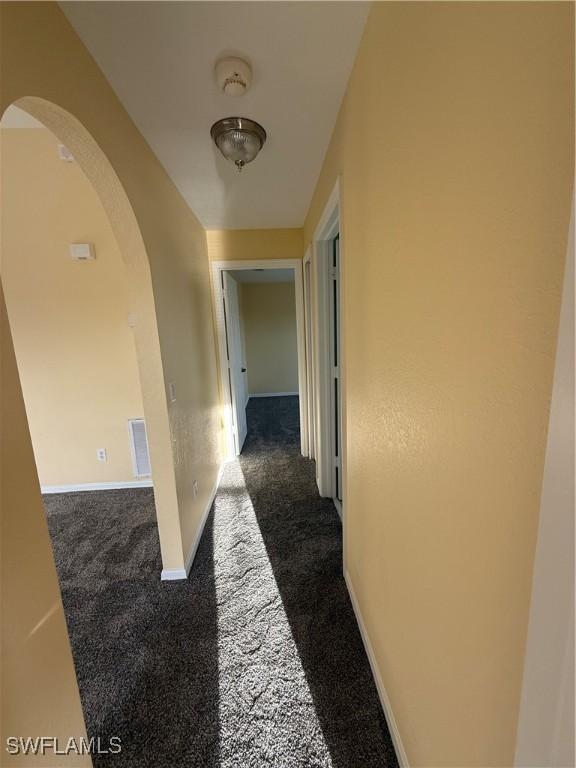 corridor featuring arched walkways, dark carpet, visible vents, and baseboards