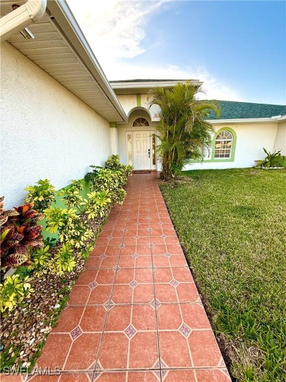 view of exterior entry with a lawn and stucco siding