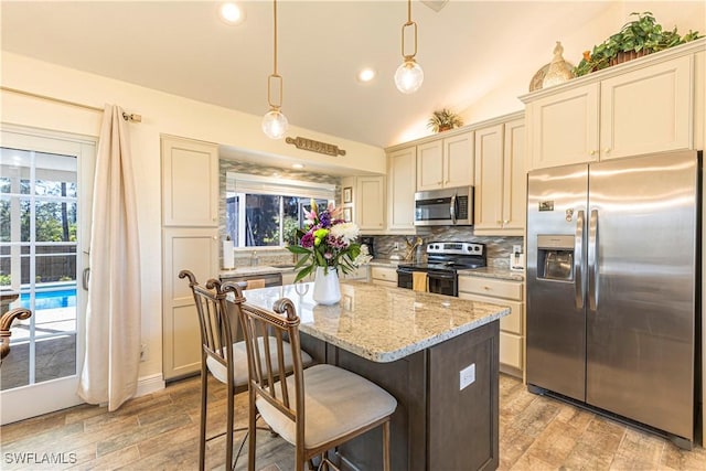 kitchen with light stone countertops, a kitchen island, lofted ceiling, decorative backsplash, and appliances with stainless steel finishes