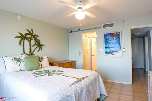 bedroom featuring visible vents, a ceiling fan, a barn door, light tile patterned floors, and baseboards