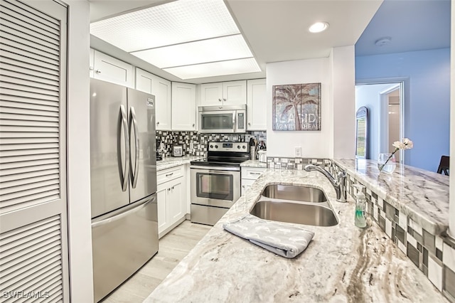 kitchen featuring light stone counters, a sink, appliances with stainless steel finishes, light wood-type flooring, and decorative backsplash