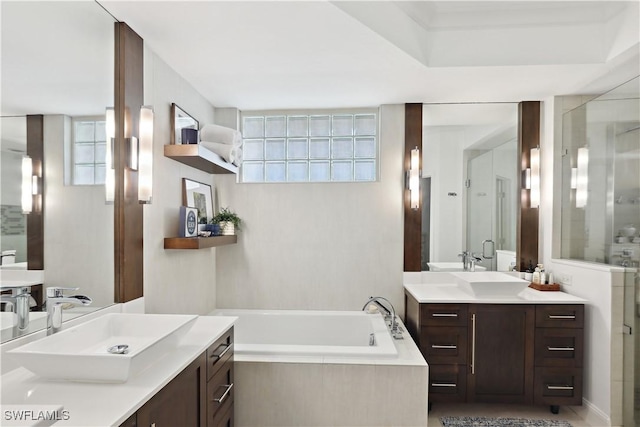 full bath featuring two vanities, a garden tub, a shower stall, and a sink