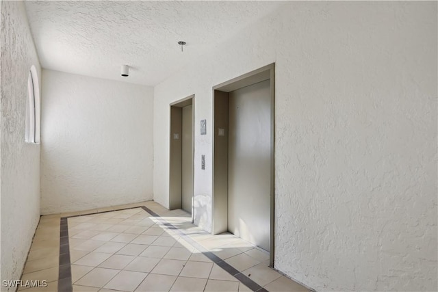 interior space featuring elevator, light tile patterned floors, a textured ceiling, and a textured wall