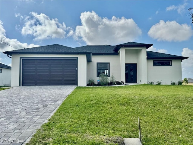 prairie-style home with an attached garage, stucco siding, decorative driveway, and a front yard