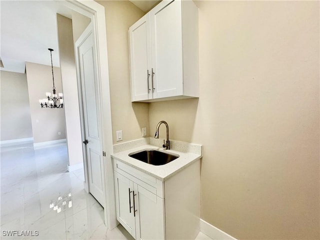 bar with a notable chandelier, a sink, baseboards, marble finish floor, and decorative light fixtures